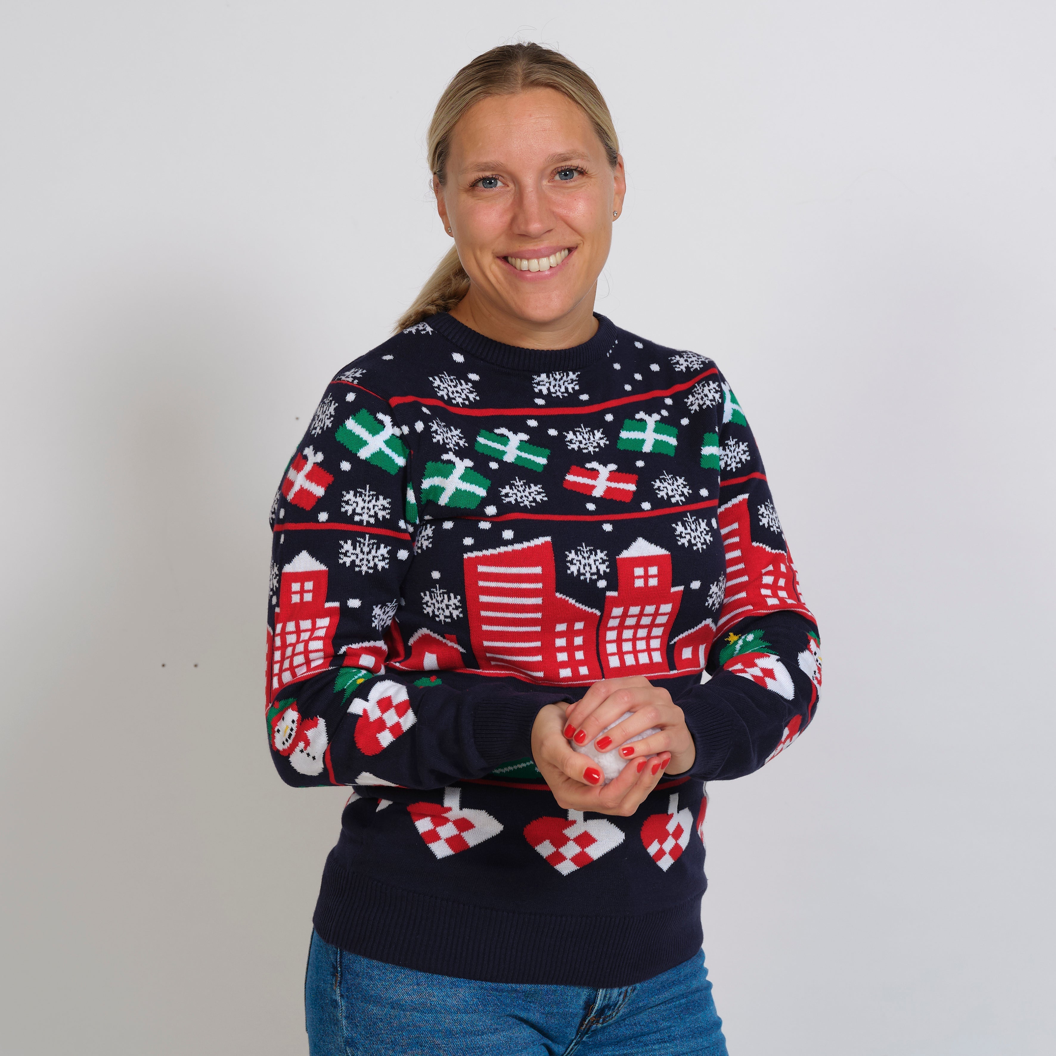 En dame iført en julesweater med gaver, snefnug og huse på.